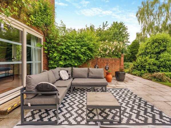 A patio with a grey sectional sofa, a patterned rug, and a small table.