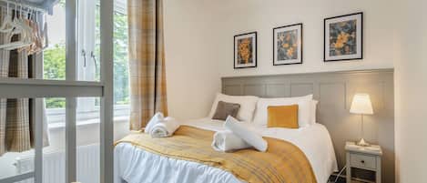 A neatly made bed with a white and yellow striped blanket, a bedside lamp, and a small bedside table.