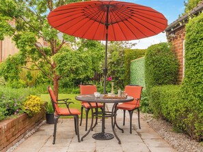 Un patio con una mesa redonda, cuatro sillas y un paraguas rojo.
