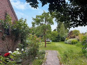 A brick building with a garden path leading to a grassy area with trees and flowering plants.
