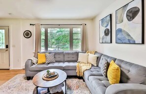 A modern living room with a grey sectional sofa, a round coffee table, and a large window with curtains. - Home w/ Hot Tub! 5 Mins from Hunter Mtn (Lanesville)