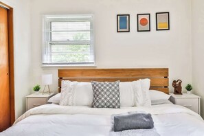 A neatly arranged bedroom with a wooden headboard, a large bed with white bedding, a bedside table with a lamp, and a window with blinds. - Home w/ Hot Tub! 5 Mins from Hunter Mtn (Lanesville)