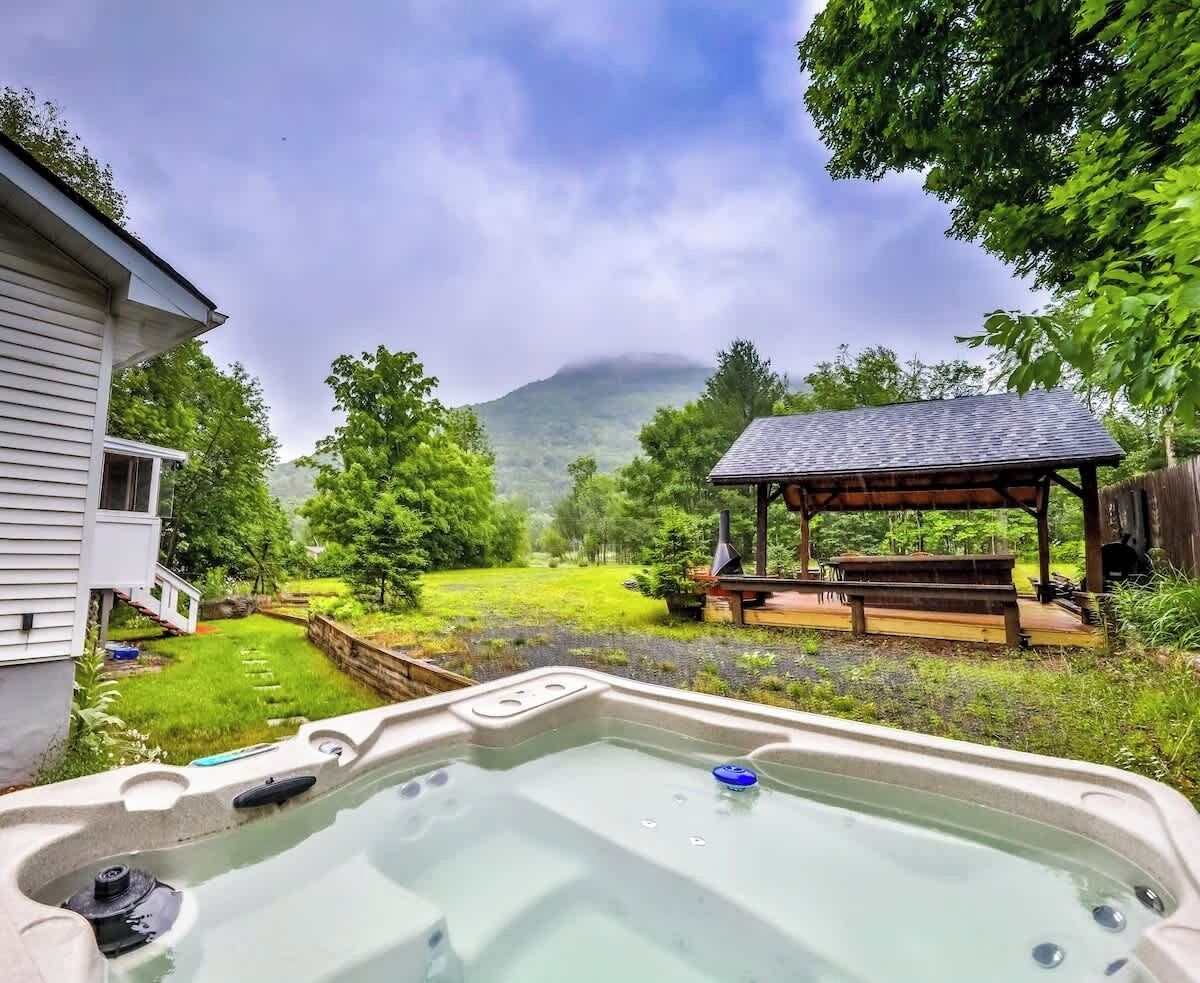 A hot tub in a backyard with a wooden deck and a gazebo in the background.
