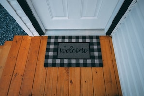 A wooden door with a black and white checkered mat and a 'Welcome' mat.
