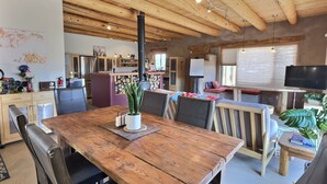 A rustic interior with a wooden dining table, chairs, a kitchen area, and a living space with a TV and seating. - Adobe Tranquillo Mountain Views (El Prado)