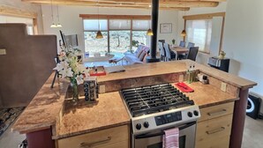A modern kitchen with a central island, a stove, and a dining area with a view. - Adobe Tranquillo Mountain Views (El Prado)