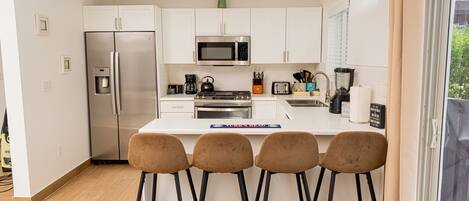 A modern kitchen with white cabinets, stainless steel appliances, and a bar area with stools.