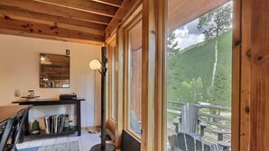 Una habitación con techo de madera, un ventanal que da a una terraza con mobiliario exterior, un espejo en la pared y una lámpara de pie.