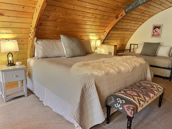 Un dormitorio acogedor con una cama grande, un banco y dos mesitas de noche con lámparas.