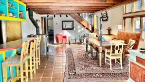 A spacious room with a wooden ceiling, a dining area with a table and chairs, a red chair, a patterned rug, and a cabinet with decorative items. - La Querencia - Taos Foothills Comfort (Arroyo Seco)