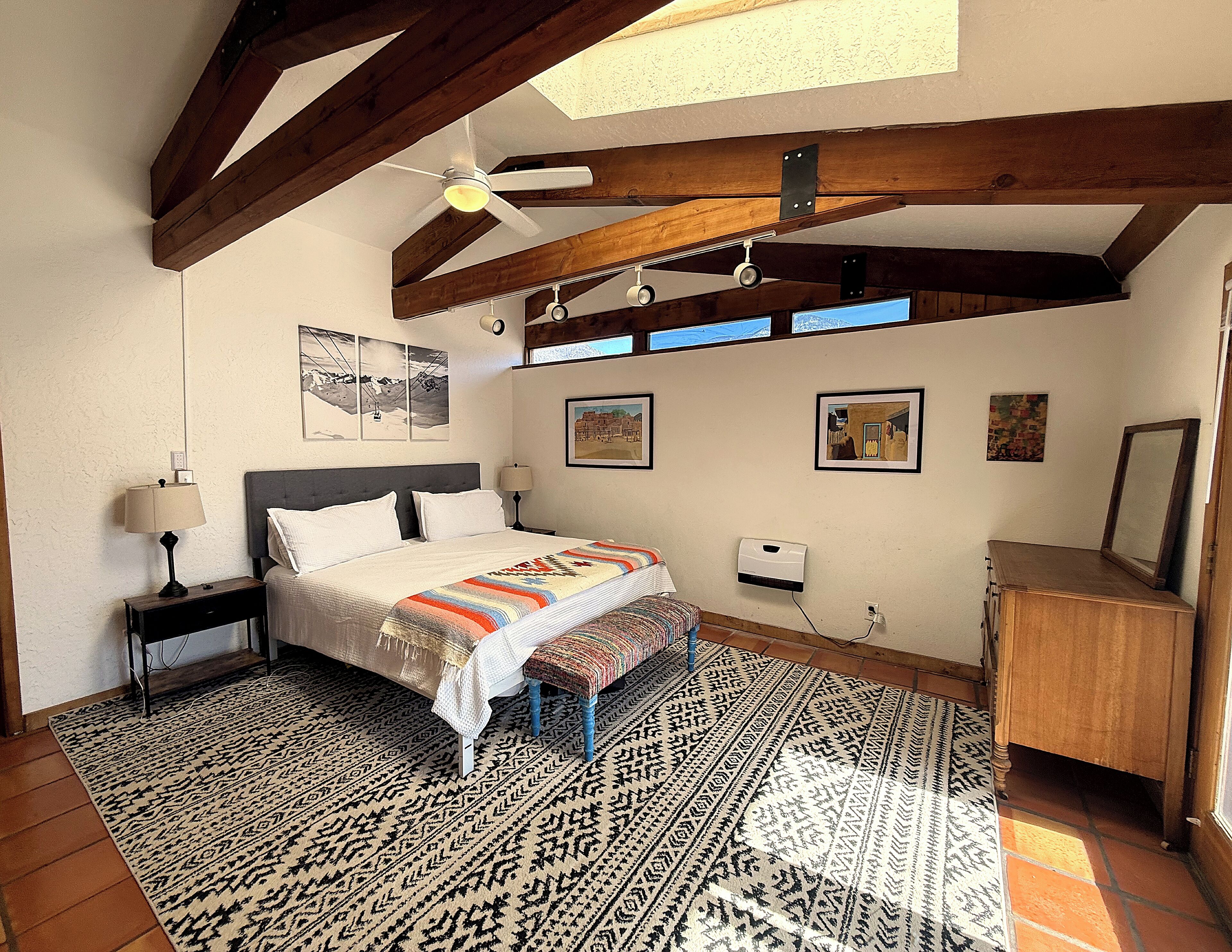 A bedroom with a bed, bedside tables, a bench, a desk, and a ceiling fan.