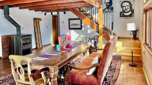 A spacious dining area with a wooden table and bench, a staircase, and a wall with a framed picture. - La Querencia - Taos Foothills Comfort (Arroyo Seco)