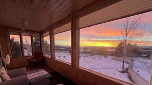 A cozy cabin room with a large window overlooking a snowy landscape at sunset. - La Querencia - Taos Foothills Comfort (Arroyo Seco)