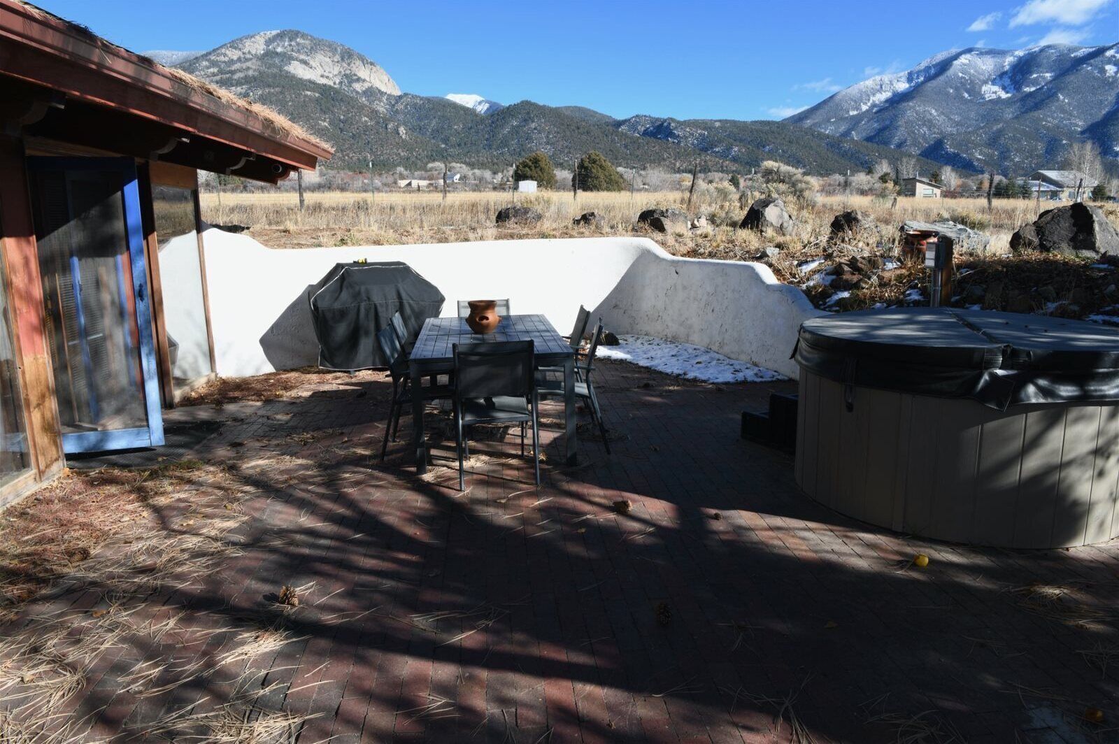A patio with a table and chairs, a hot tub, and a view of mountains.
