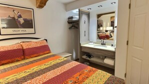 Un dormitorio con cama, un espejo grande, un baño con lavabo y un cuadro en la pared.