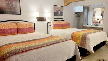 Habitación de hotel con dos camas, cada una con almohadillas estampadas y una colcha. Hay lámparas fijadas a la pared y un cuadro enmarcado sobre las camas.