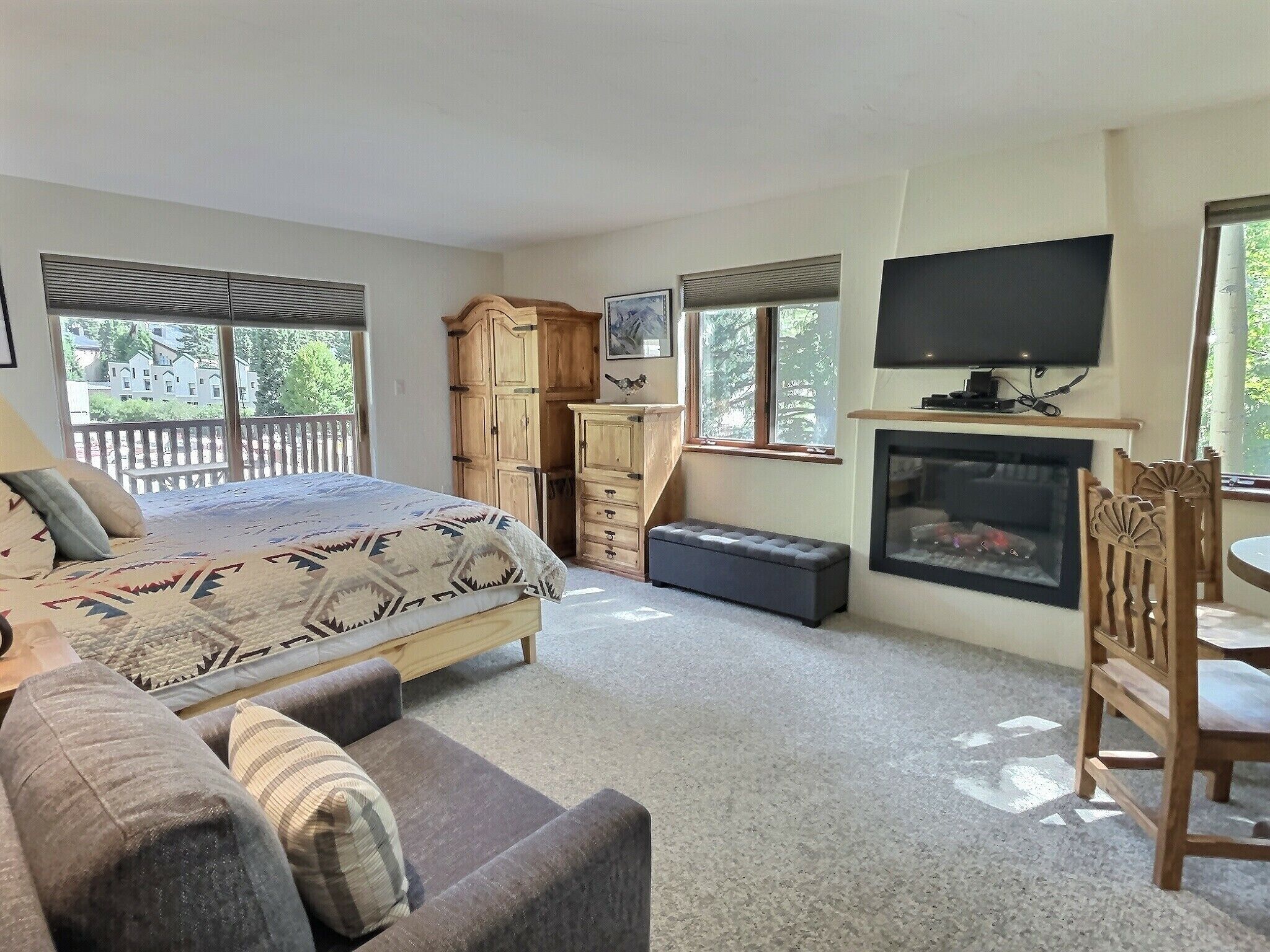 A bedroom with a bed, a sofa, a wooden wardrobe, a television, and a fireplace.