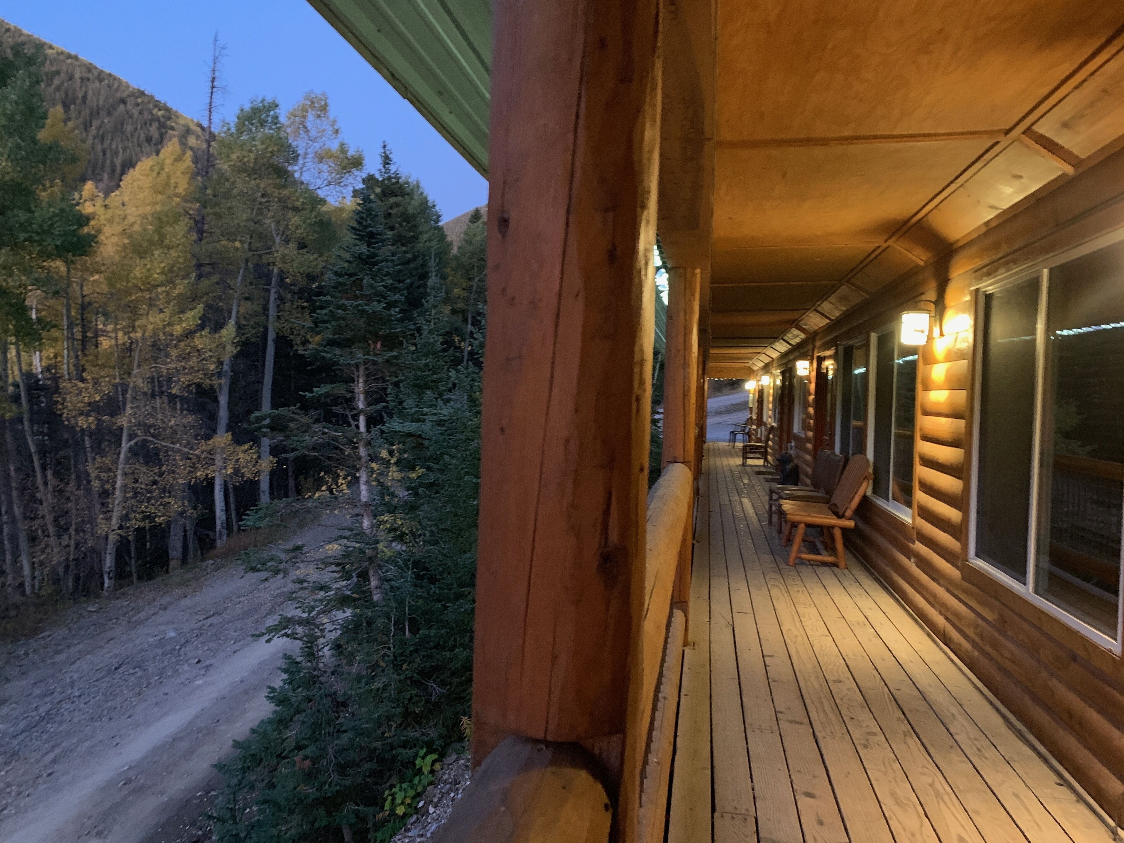 Eine Holzhütte mit Veranda, einem Feldweg und einem bewaldeten Berg im Hintergrund.