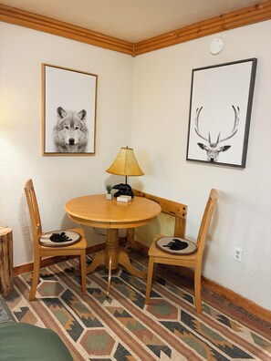 A dining area with a round wooden table, two chairs, a lamp, and two framed pictures on the wall. - Backcountry Haven at the Snow Bear at Taos Ski Valley (Taos Ski Valley)