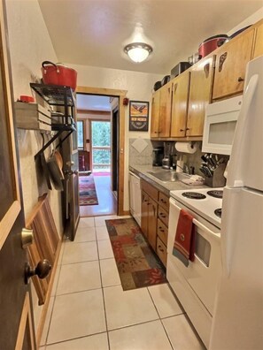 Una cocina compacta con armarios de madera, microondas, estufa y refrigerador. Una olla roja está sobre la estufa, y un bolso rojo cuelga en la puerta.