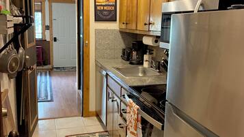 A kitchen with wooden cabinets, a stainless steel refrigerator, a coffee maker, and a patterned rug.