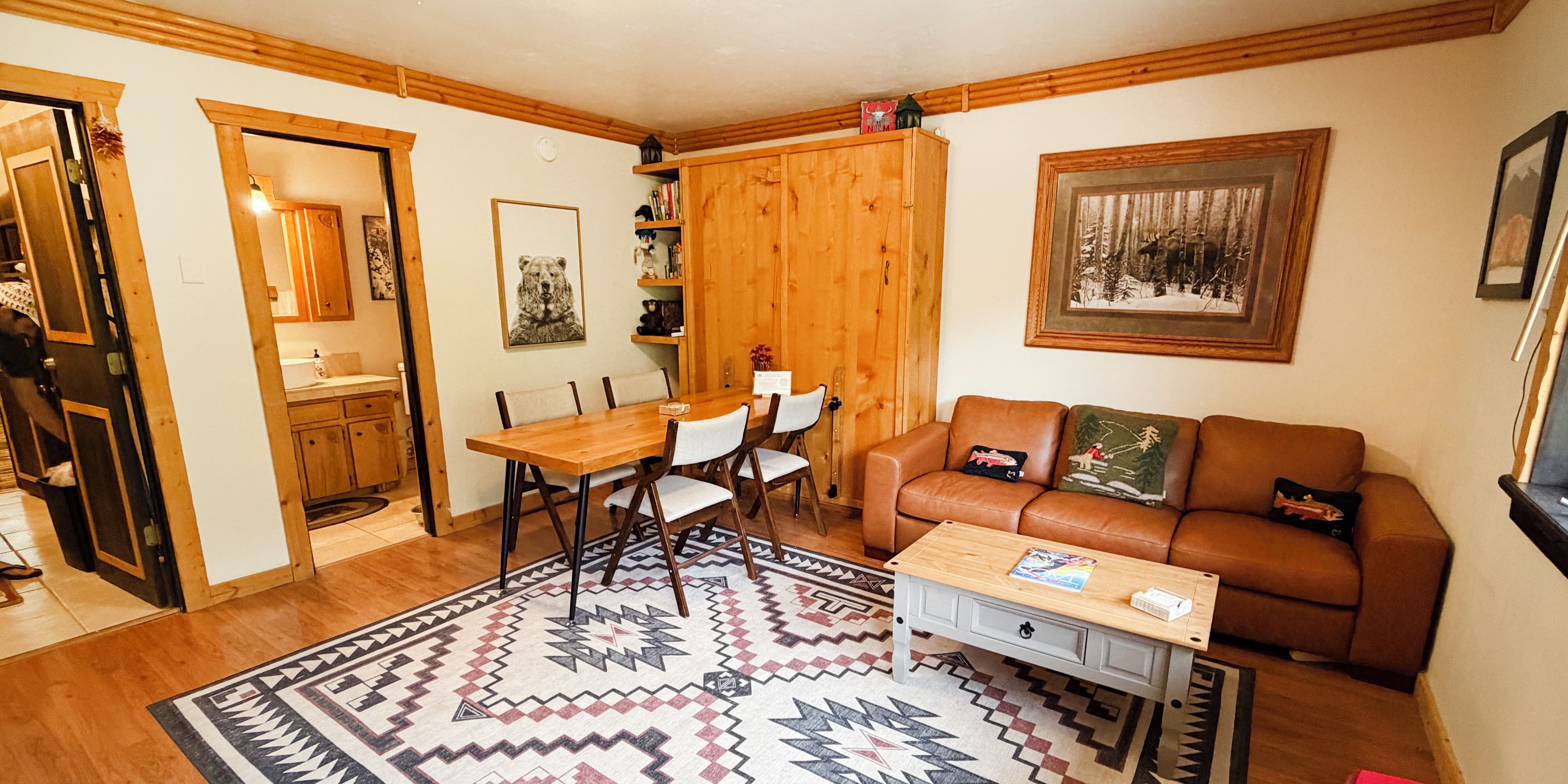 Una sala de estar acogedora con una mesa de comedor de madera, un sofá de cuero marrón y un tapete estampado.