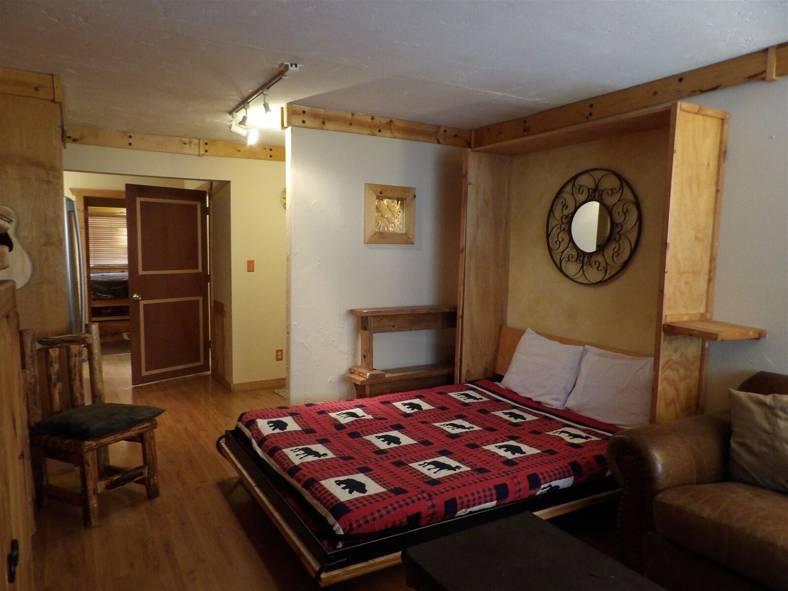 A bedroom with a bed, a wooden bench, a chair, a mirror, and a door leading to another room.