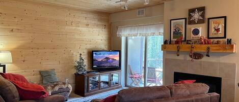 Una sala de estar acogedora con chimenea, paredes de madera, un televisor y un balcón con mobiliario exterior.