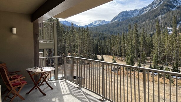 A balcony with a table and chairs, overlooking a mountainous landscape with dense forests and snow-capped peaks. - High Altitude Gem at Taos Ski Valley (Taos Ski Valley)