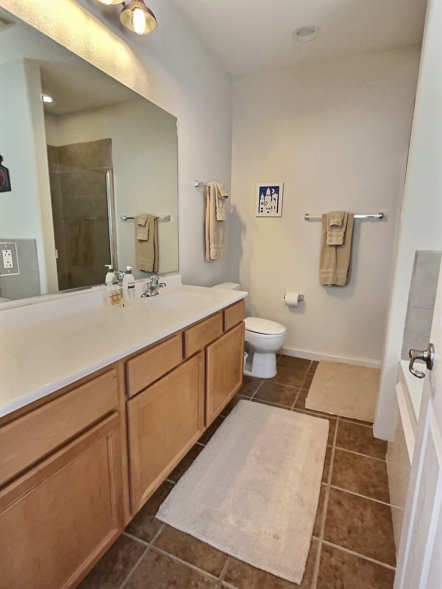 A bathroom with a large mirror, a sink, a toilet, and a shower.
