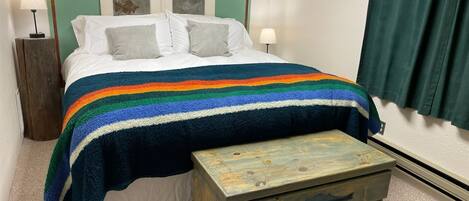 Un dormitorio con cama, mesita de noche, cómoda y cuadros en la pared.