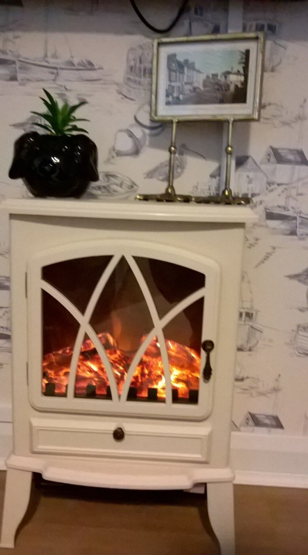 A white wood-burning stove with a glass door, a small plant on top, and a framed picture above it.