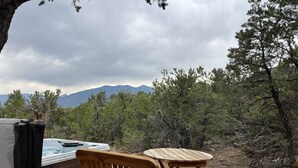 A hot tub with a wooden table and chairs, surrounded by trees and mountains in the background. - Beautiful Adobe in the Pines Above Taos (Taos)