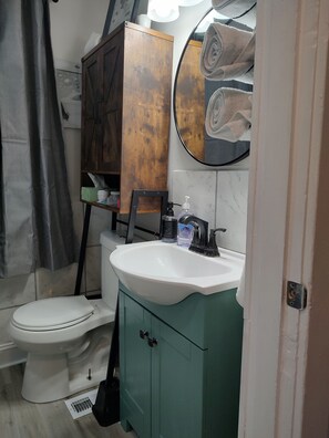 Un bagno con un water bianco, un armadietto verde, un lavandino bianco con uno specchio sopra e un porta asciugamani con asciugamani.