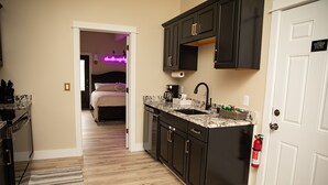 A modern kitchen with dark cabinets, a marble countertop, and a white door.