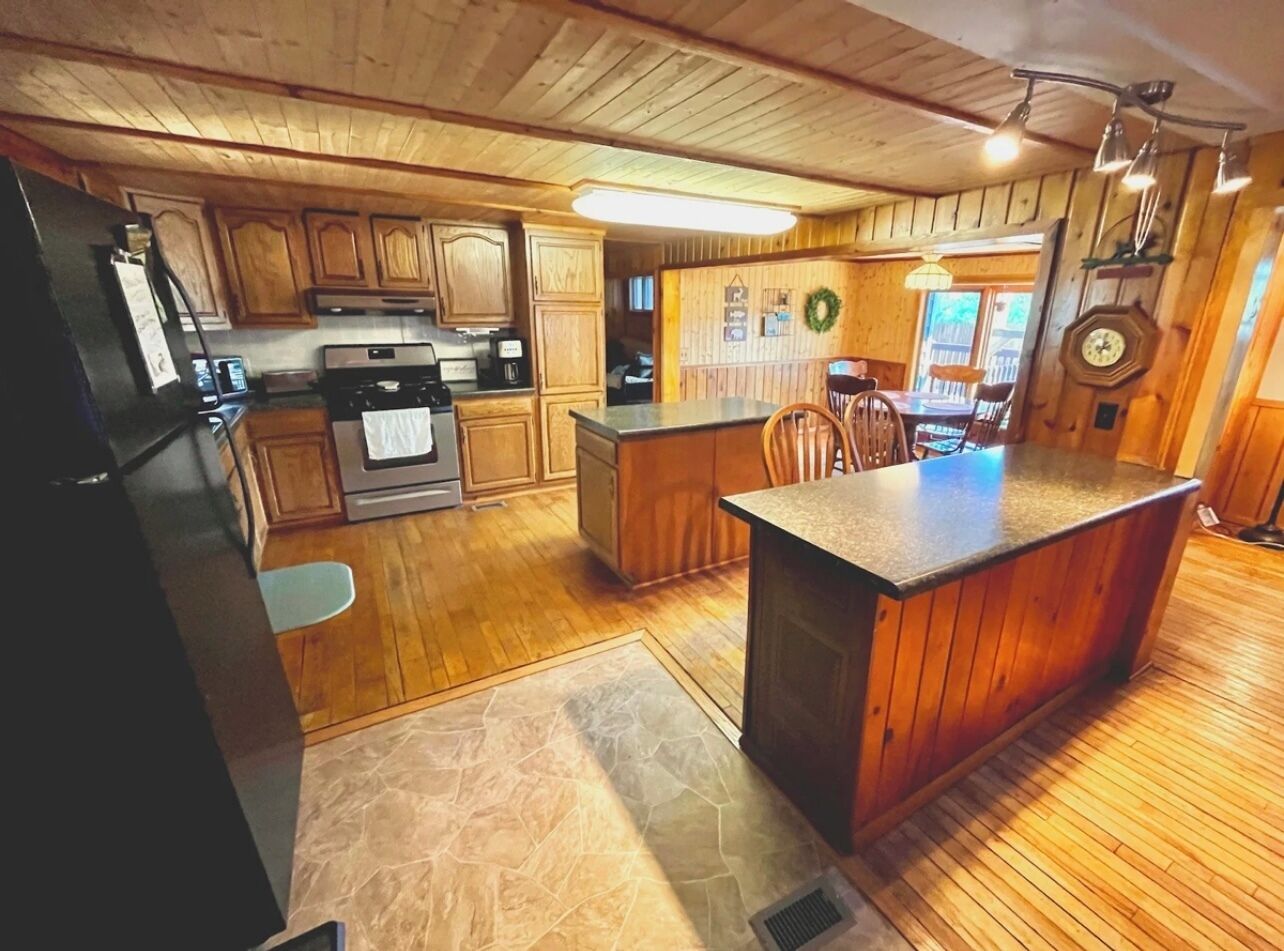A kitchen with wooden cabinets, a central island, and a dining area with chairs.