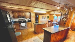 A kitchen with wooden cabinets, a central island, and a dining area with chairs. - Cozy 3 b/r home w/ quick access to snowmobile trails in the beautiful Northwoods (Minocqua)