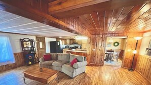 A spacious living area with a wooden floor, a sofa, a coffee table, and a kitchen in the background. - Cozy 3 b/r home w/ quick access to snowmobile trails in the beautiful Northwoods (Minocqua)