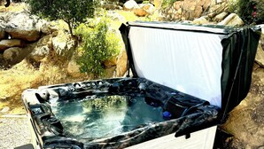 Ett portabelt bubbelbad med en träpanel på utsidan och en vit inredning, placerat på ett grusunderlag utomhus.