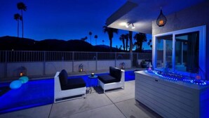 Un espace extérieur aménagé en terrasse, avec une piscine, des chaises longues et un bar éclairé de lumières bleues.
