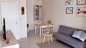 A modern living room with a grey sofa, a small round table, and a white TV stand.