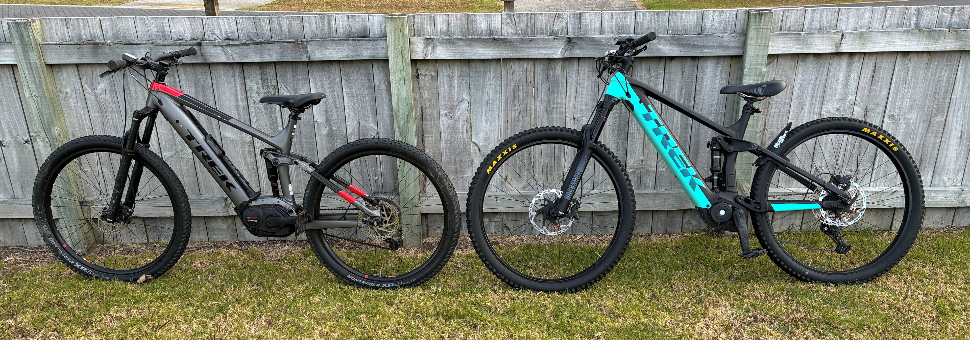 Two bicycles parked against a wooden fence.