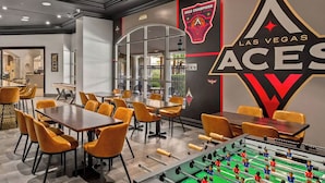 A modern indoor space with multiple tables and chairs, a foosball table, and a wall with the Las Vegas Aces logo. - Wyndham Grand Desert 2 BR Deluxe - Full Resort Access 1 Mile of Vegas Strip! (Las Vegas)