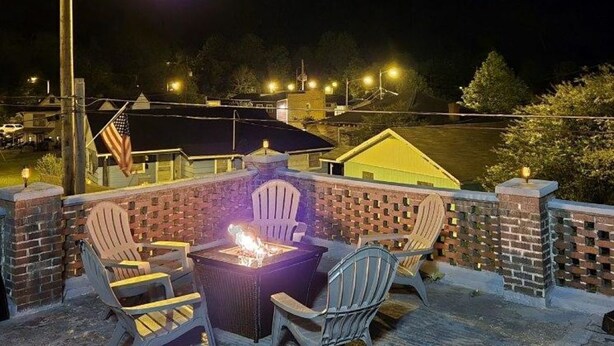 Un patio con paredes de ladrillo, un brasero y sillas Adirondack.