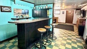 Una zona de bar con suelo a cuadros, una barra con taburetes y una pared decorada con marcos.
