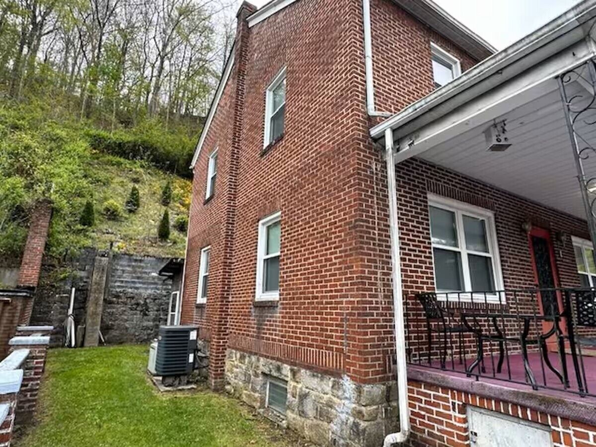 A two-story brick house with a stone foundation, a covered porch, and a small front yard.