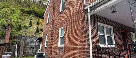 A two-story brick house with a stone foundation, a covered porch, and a small front yard.