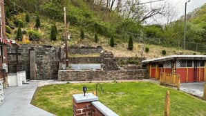 Un patio trasero con muro de ladrillo, un pequeño estanque y valla de madera.
