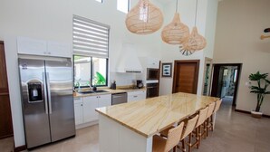 A modern kitchen with stainless steel appliances, a marble island, wicker chairs, and woven pendant lights.