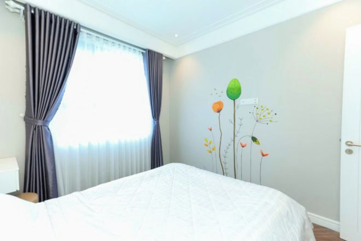 A bedroom with a bed, a window with curtains, and a wall with a floral mural.